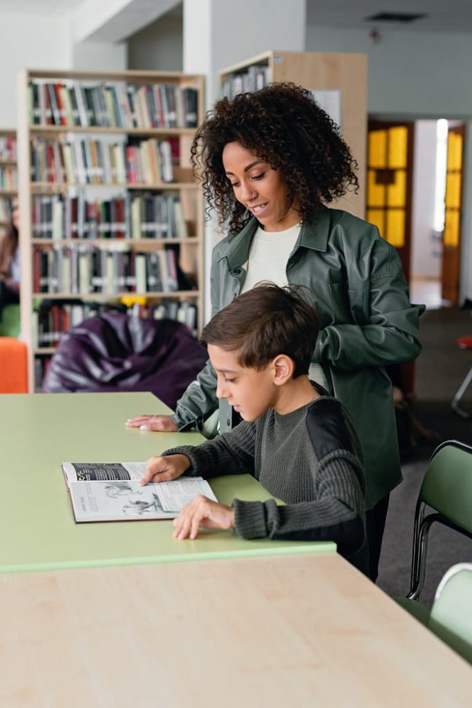 A teacher helps a student with reading in a library environment.