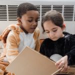 Two children reading a book together in cozy animal costumes, indoors.